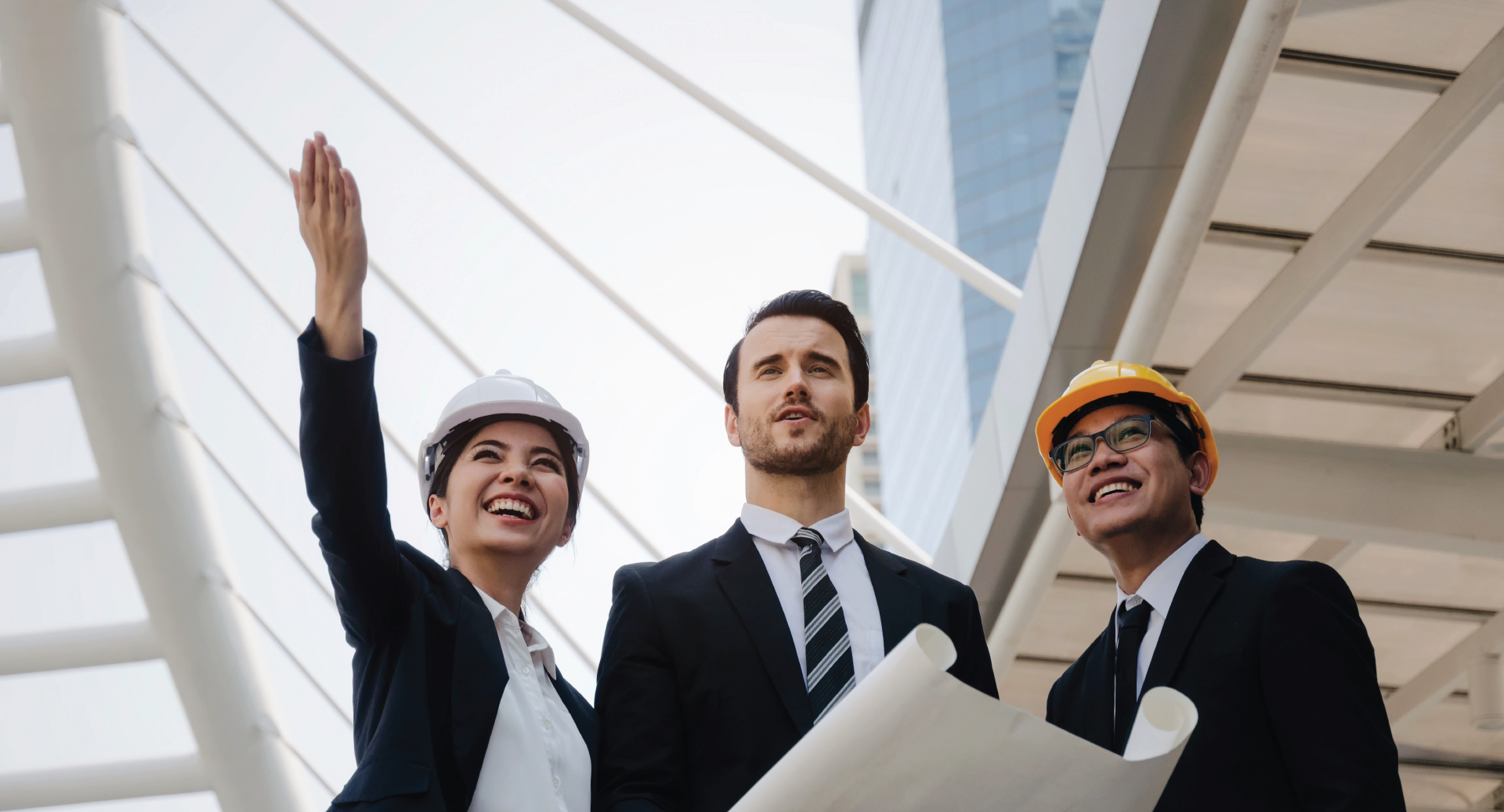 Three professionals in hard hats and business attire discuss a building project outdoors.