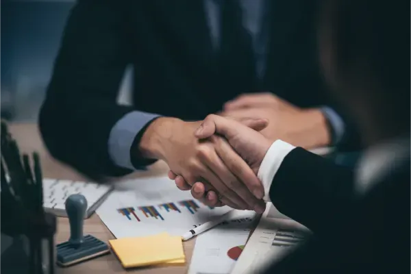 Businesspeople shaking hands over documents on a desk in a meeting room