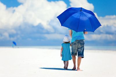 A man and a little girl are walking on the beach holding an umbrella.