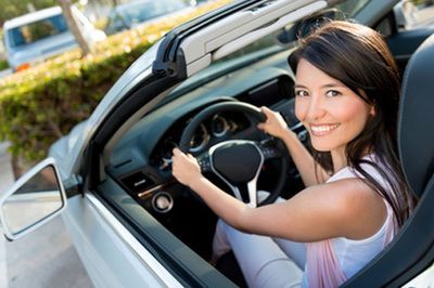 A woman is sitting in a convertible car and smiling.