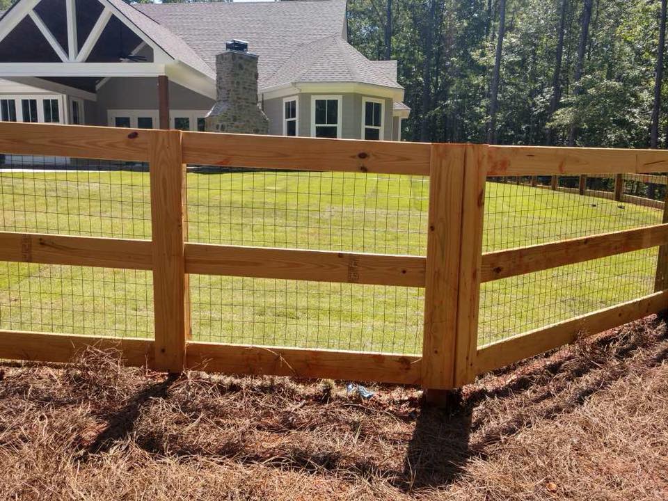 A wooden fence surrounds a lush green field in front of a house.