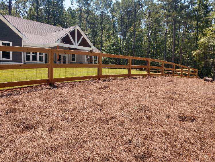 A wooden fence surrounds a large field in front of a house.