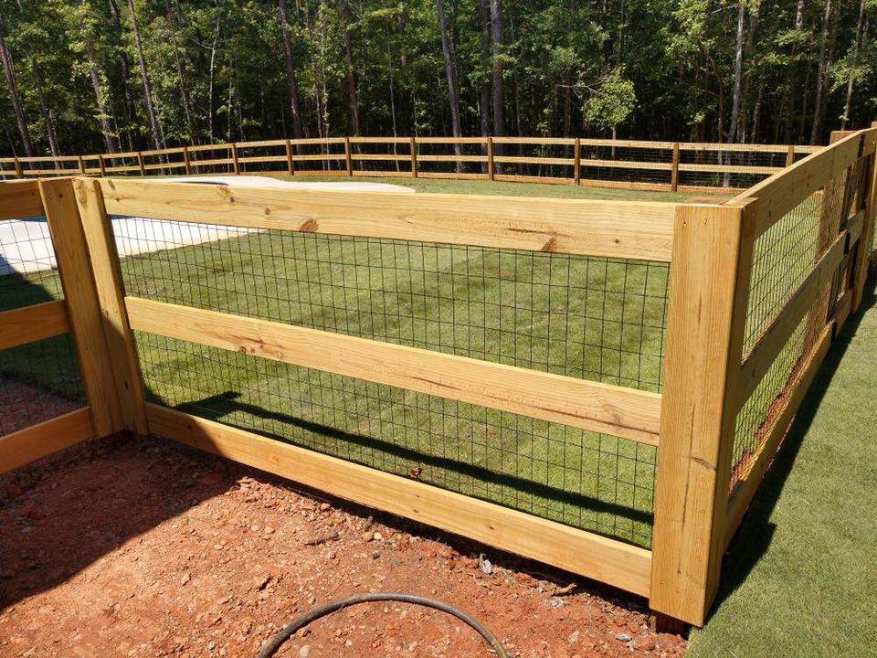 A wooden fence surrounds a lush green field.