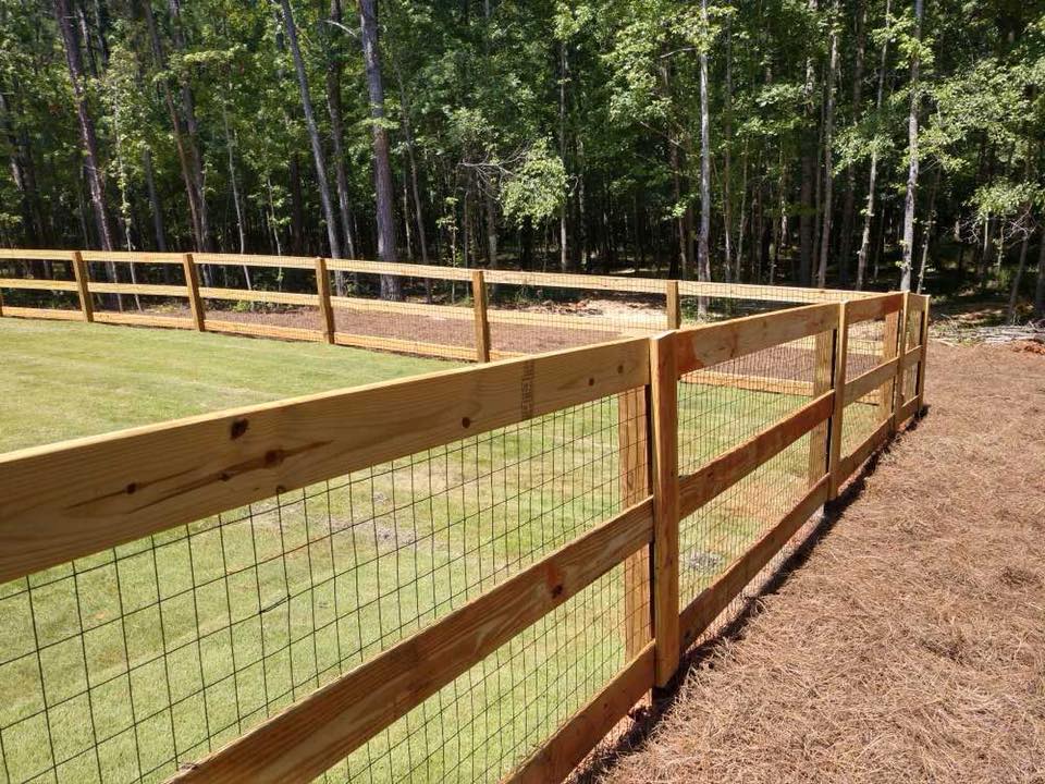 A wooden fence with a wire mesh surrounding a lush green field.