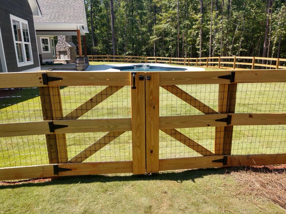 A wooden fence with a gate and a pool in the background.