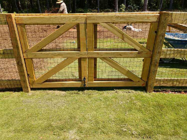 A wooden fence with a gate in the middle of a lush green field.
