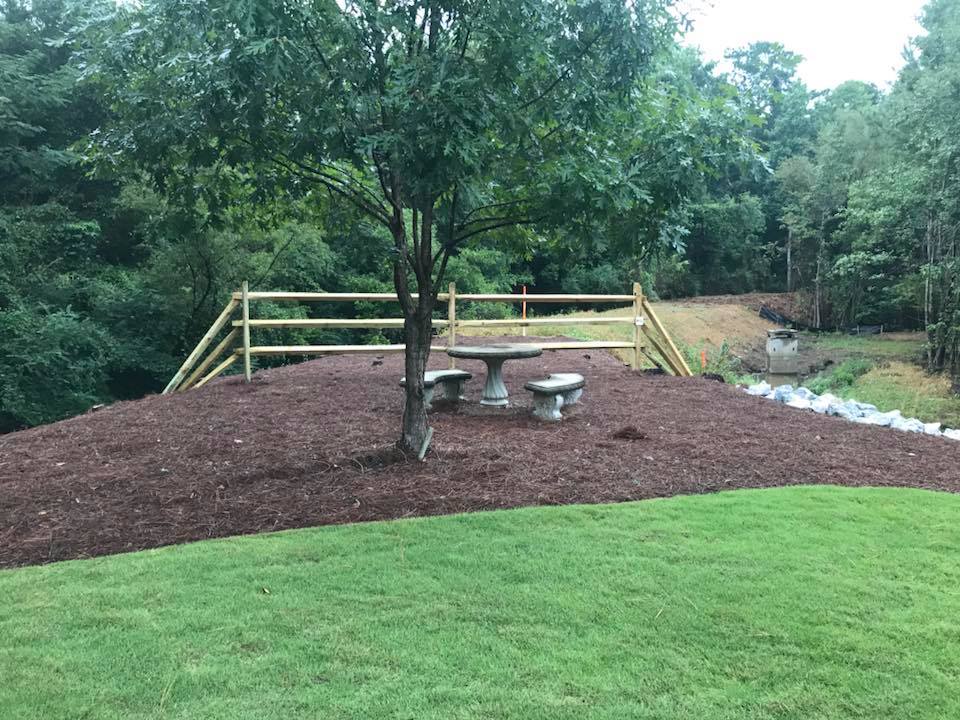 A picnic table is sitting on top of a hill next to a wooden fence.