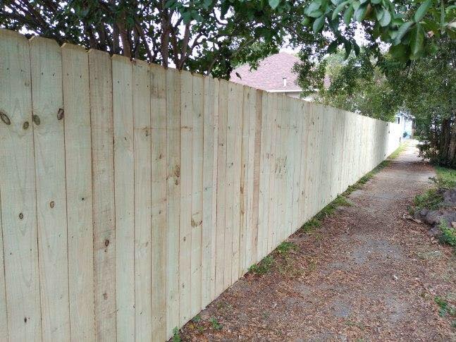 A wooden fence along a path with trees in the background.