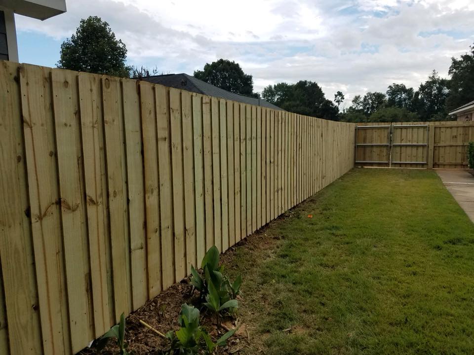 A wooden fence surrounds a lush green lawn in a backyard.