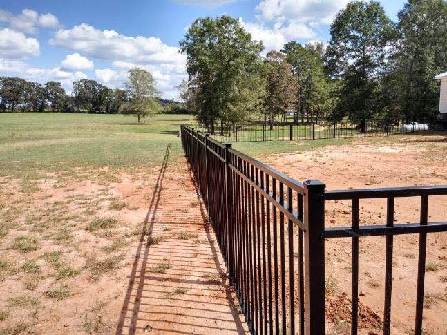 A black fence surrounds a field with trees in the background