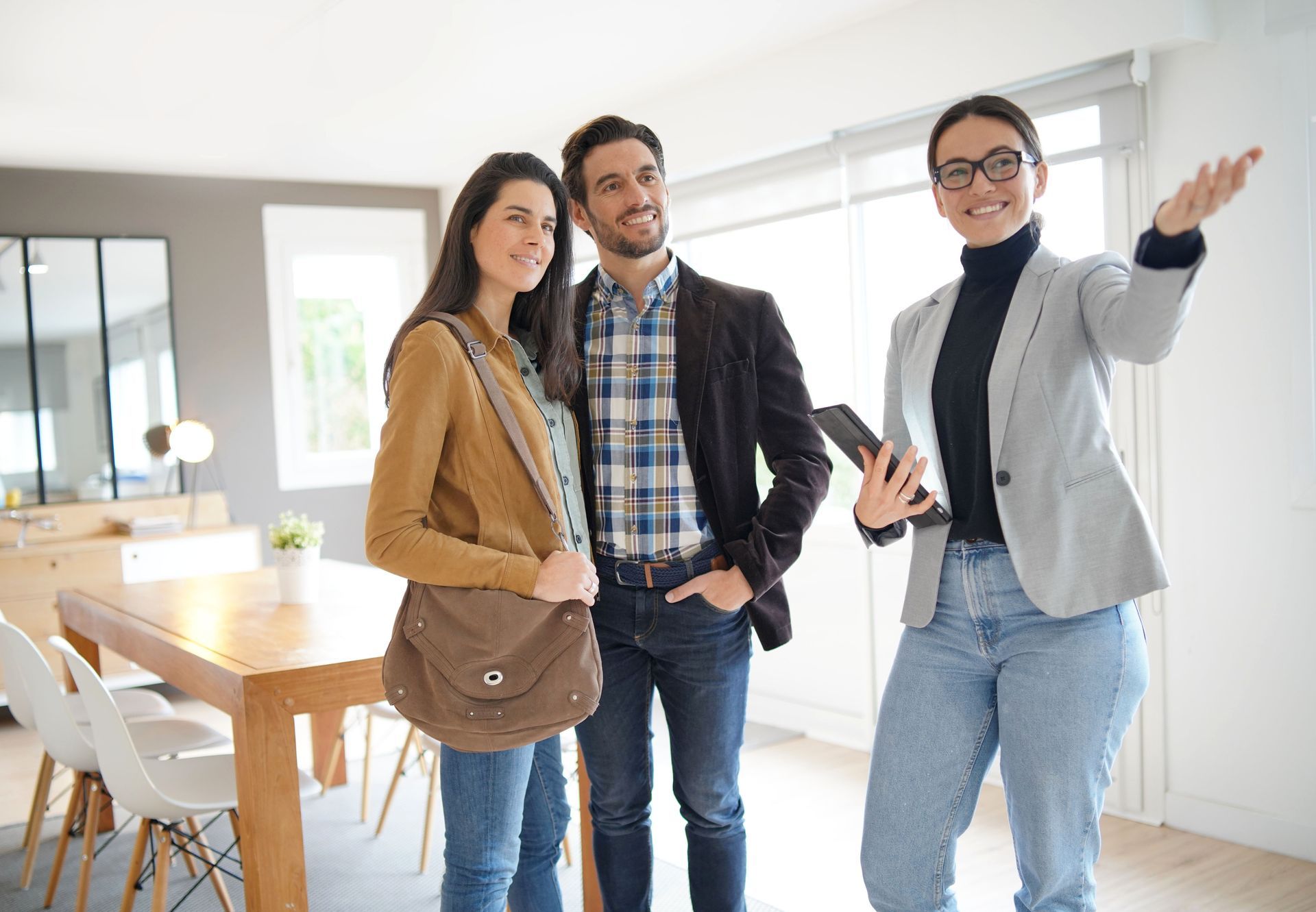 Three people standing in a bright living room, smiling and talking, one gesturing toward the space.