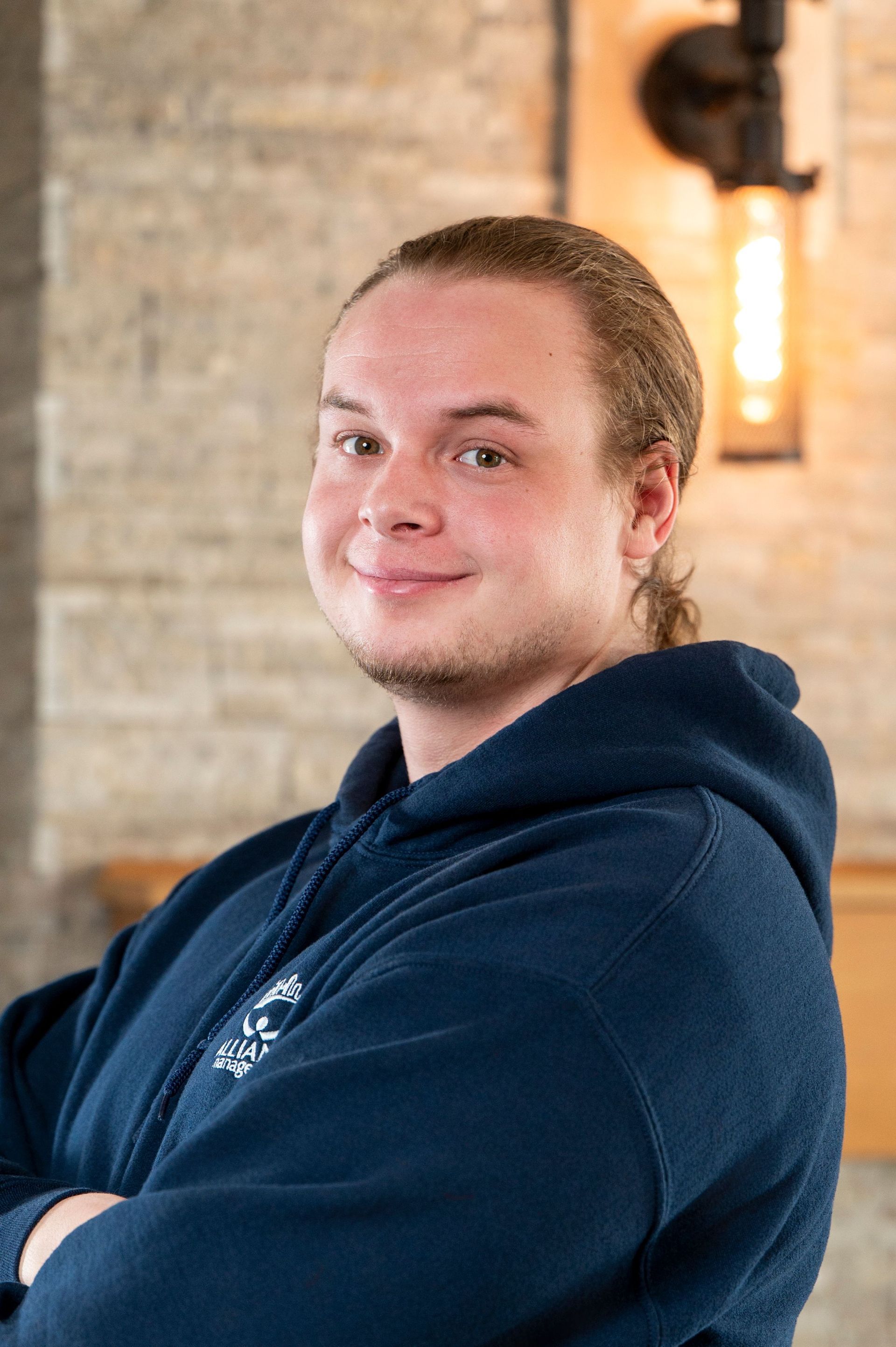 Person in a navy hoodie smiling indoors against a brick wall backdrop