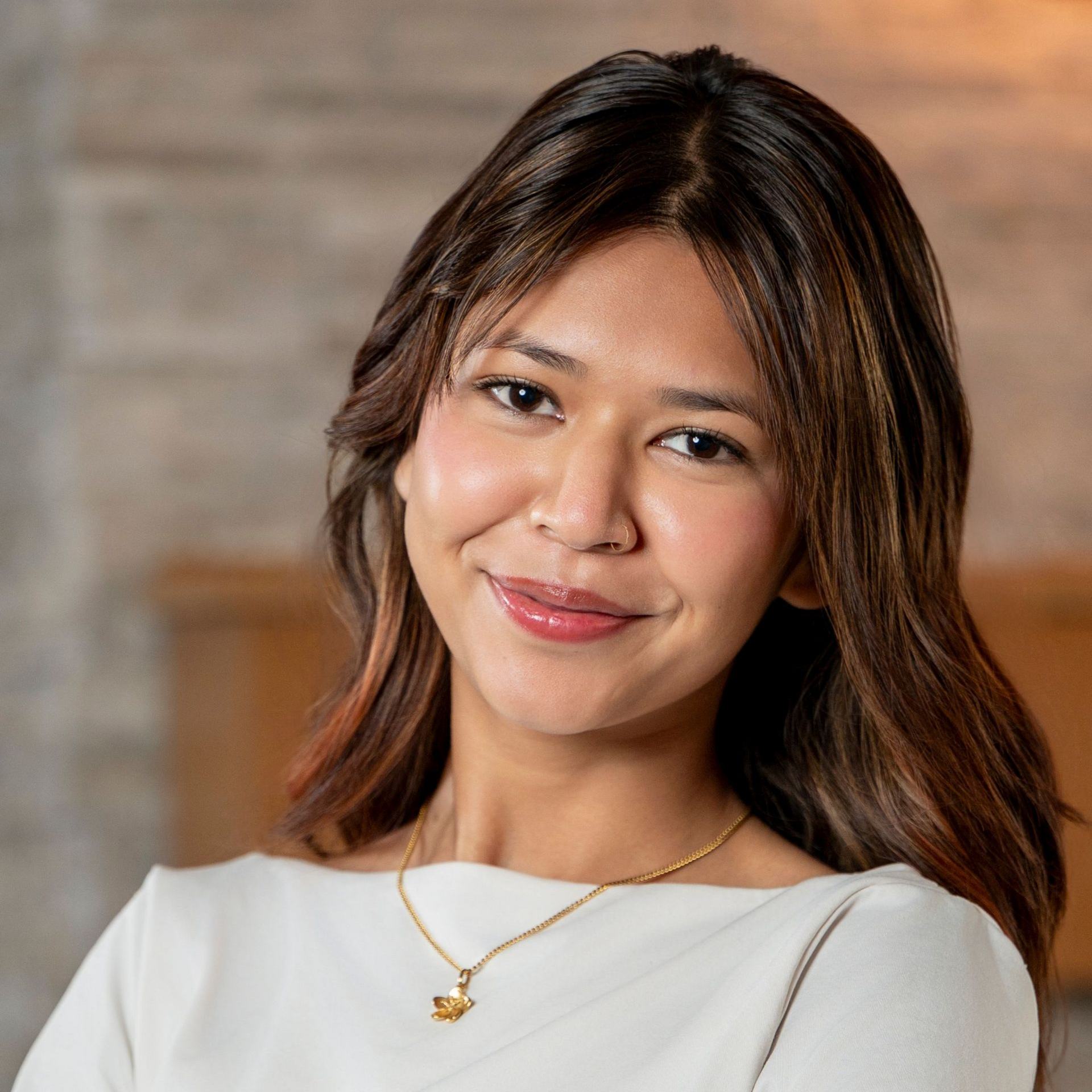 Smiling woman in a white top and gold necklace against a softly blurred brick background
