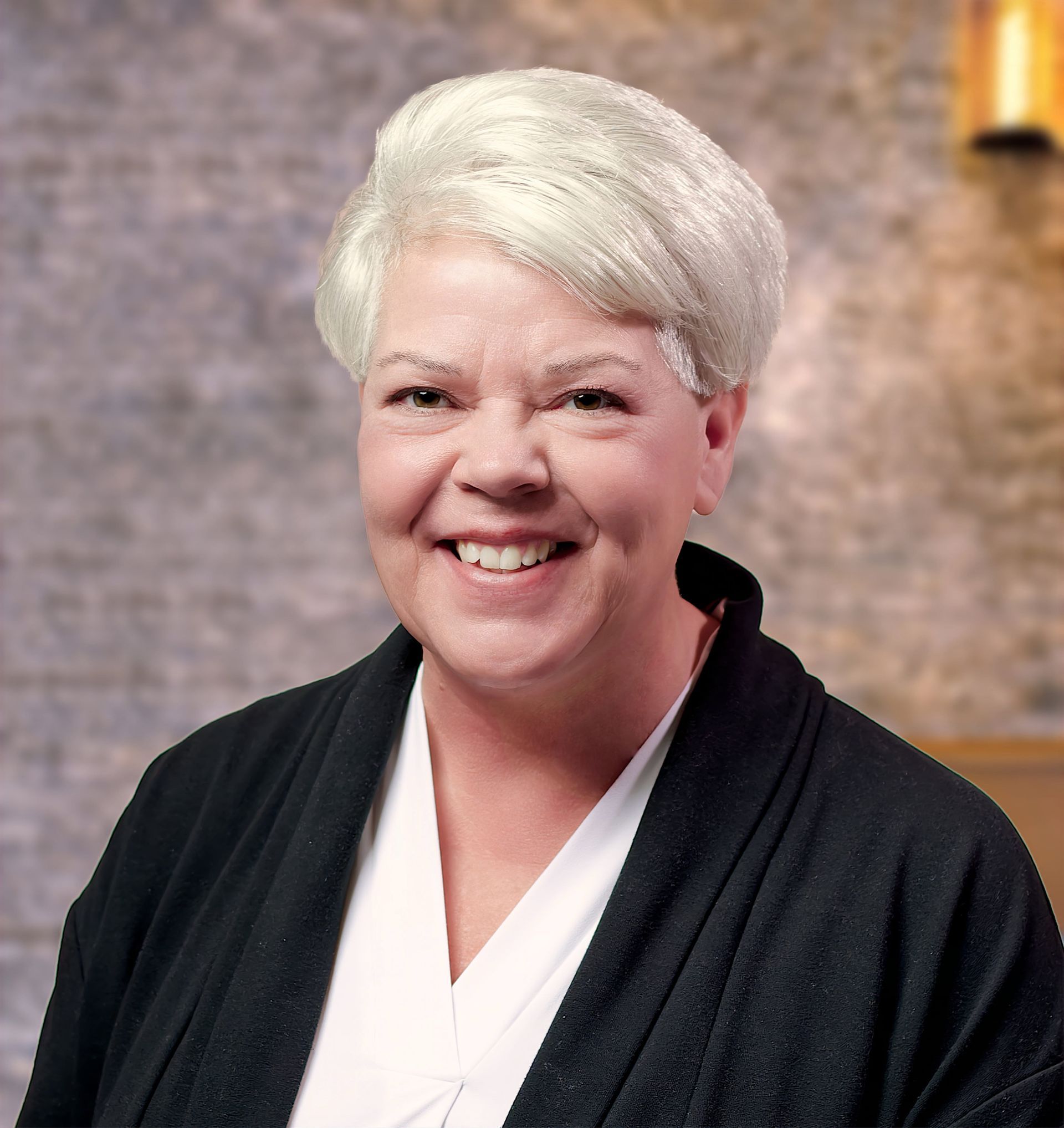 Smiling person with short white hair in a black jacket against a blurred indoor background