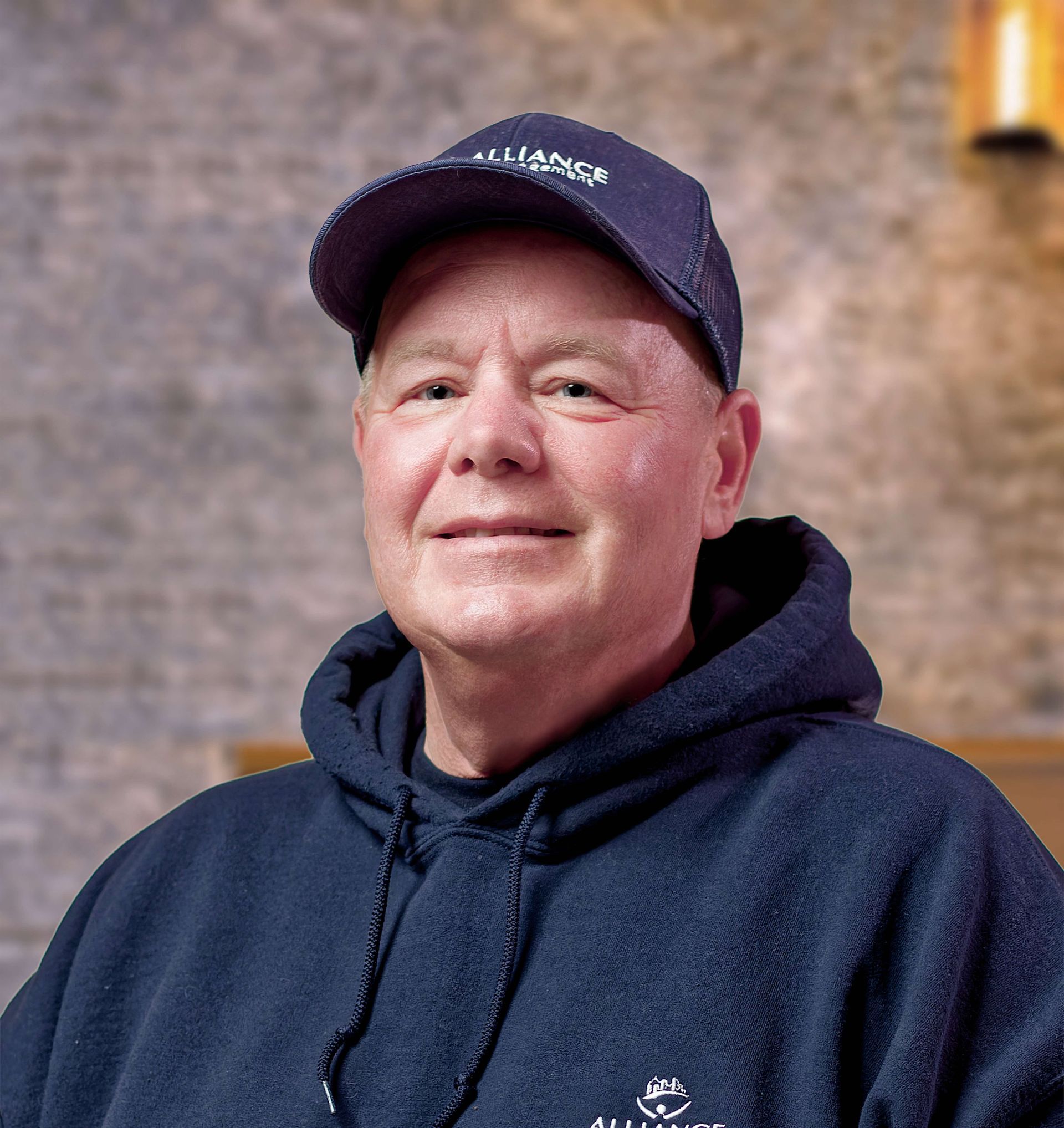 Portrait of a smiling person in a navy hoodie and cap against a warm indoor background