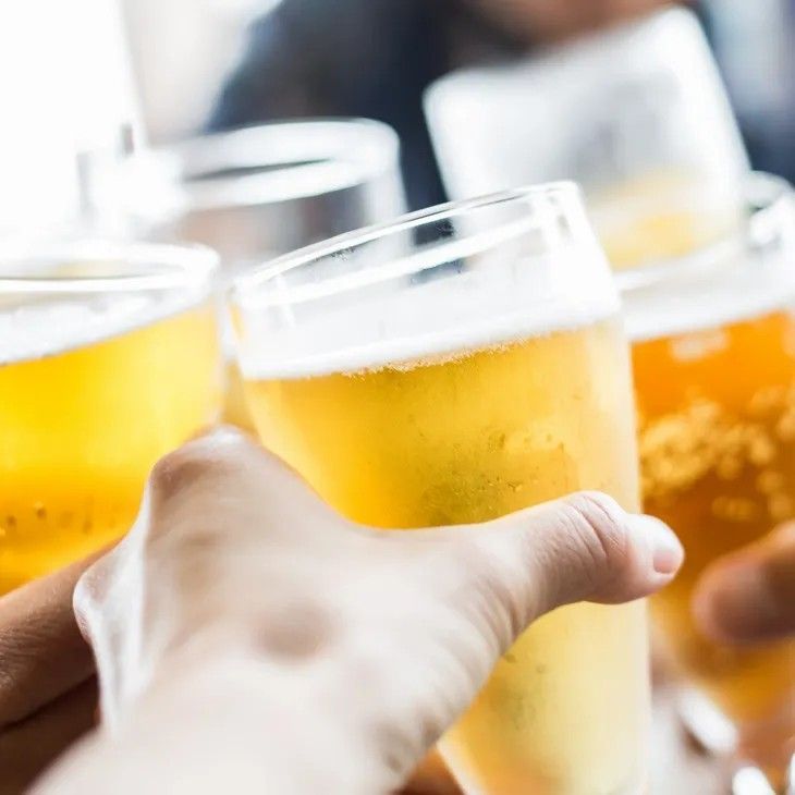 Hands toasting glasses of beer, golden yellow liquid, close-up, indoors, blurred background.