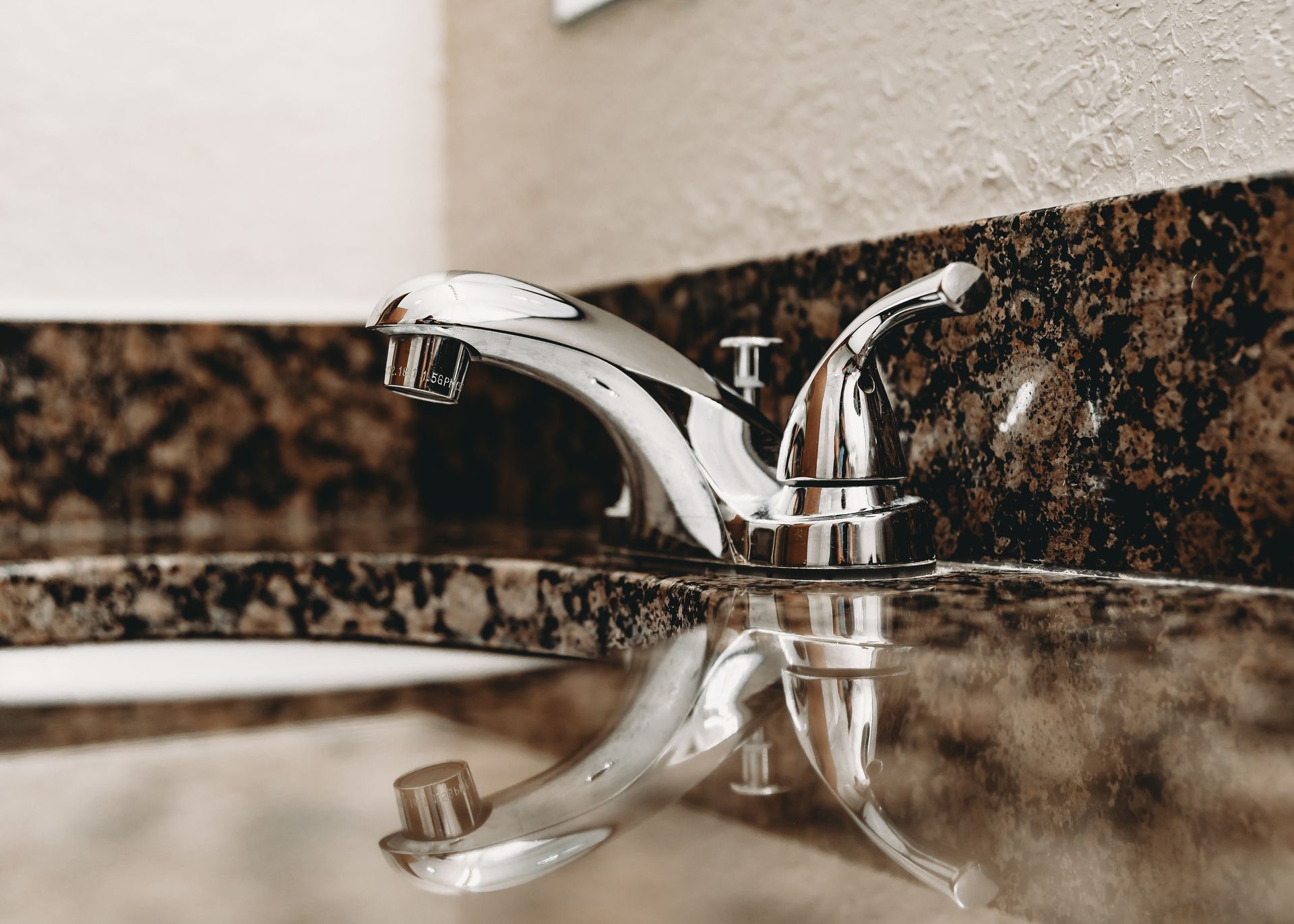Chrome faucet on a marble countertop with its reflection visible.