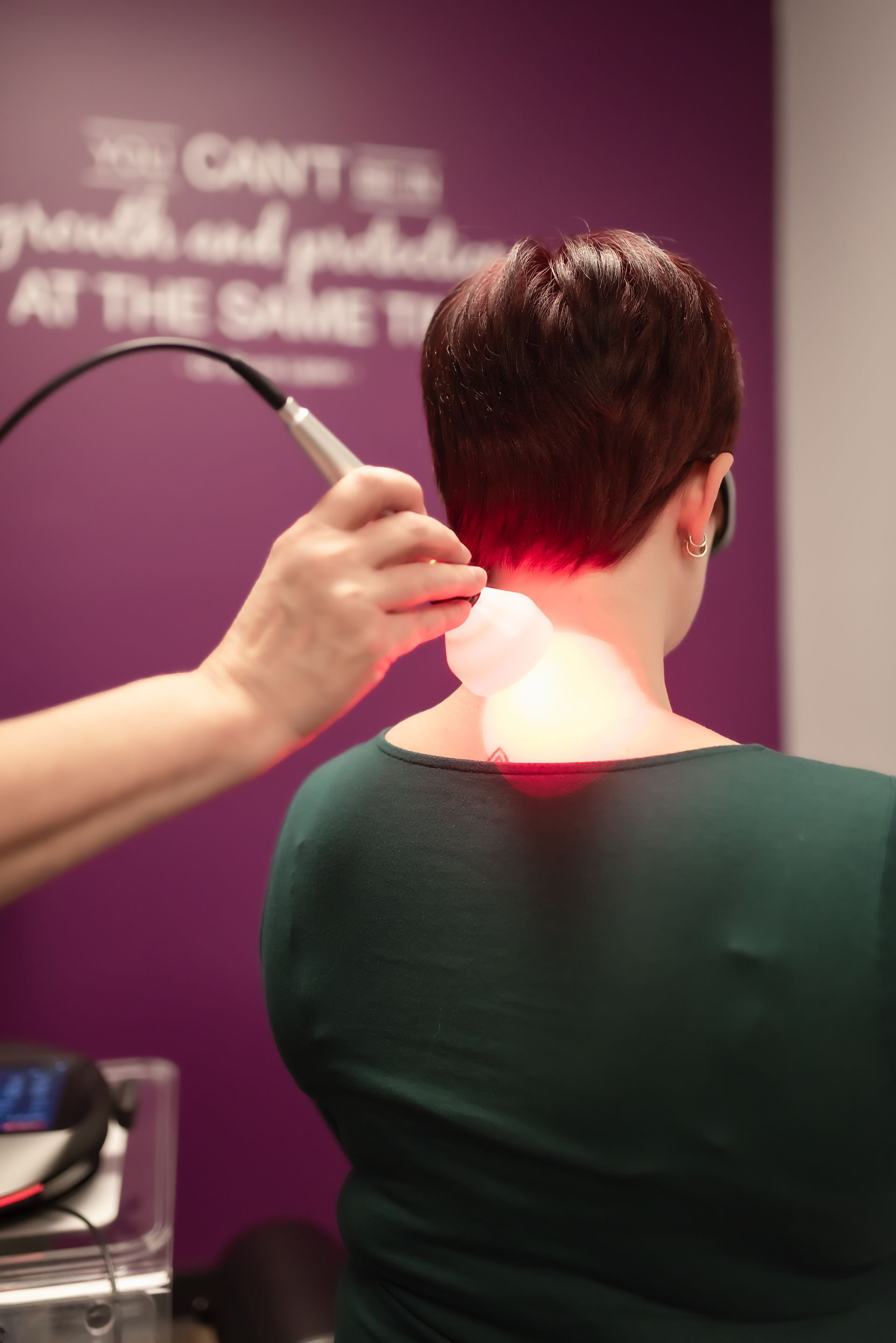 Person receiving a neck treatment with a handheld device under pink-purple light