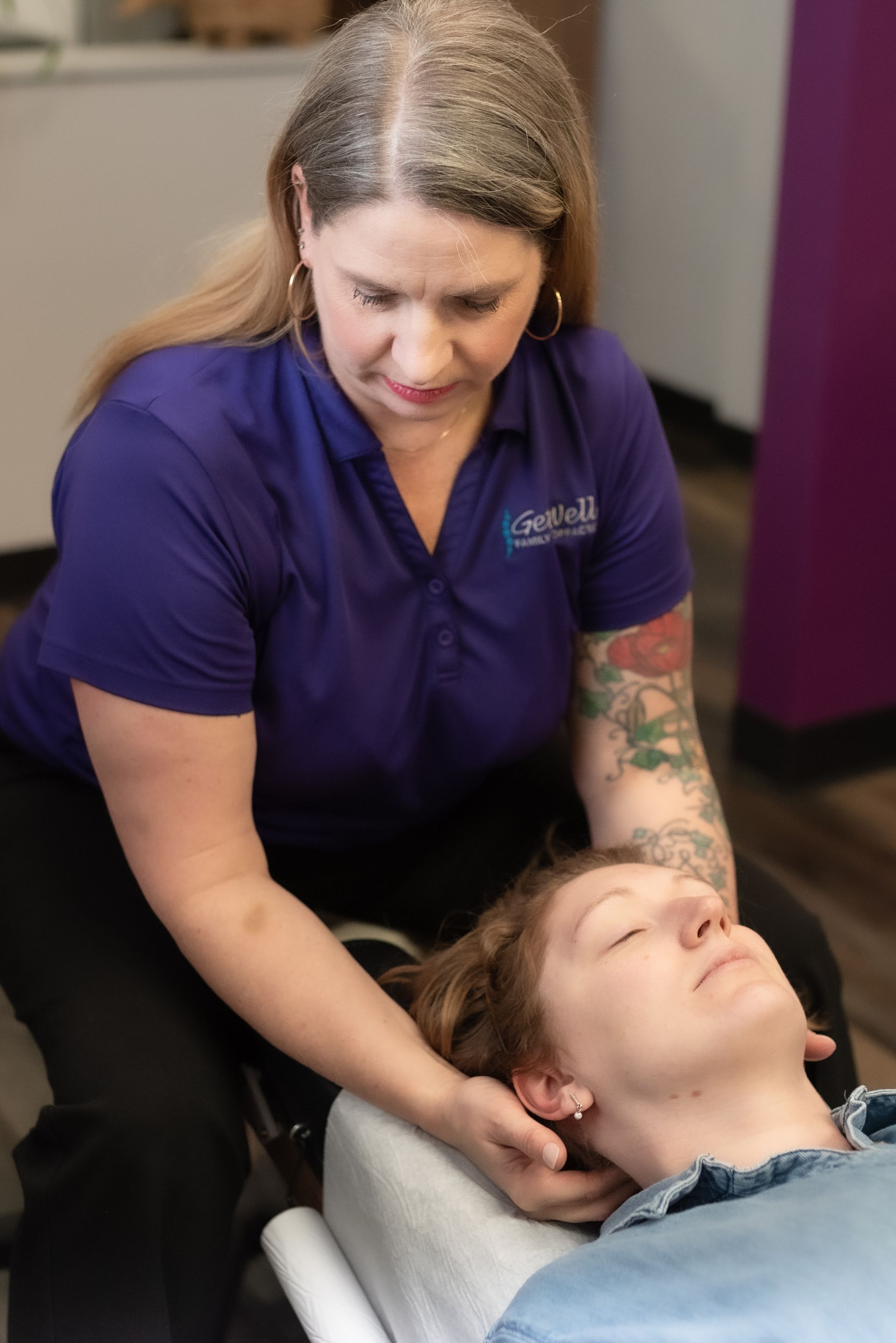 Woman in purple shirt giving a neck massage to a reclining client in a spa setting