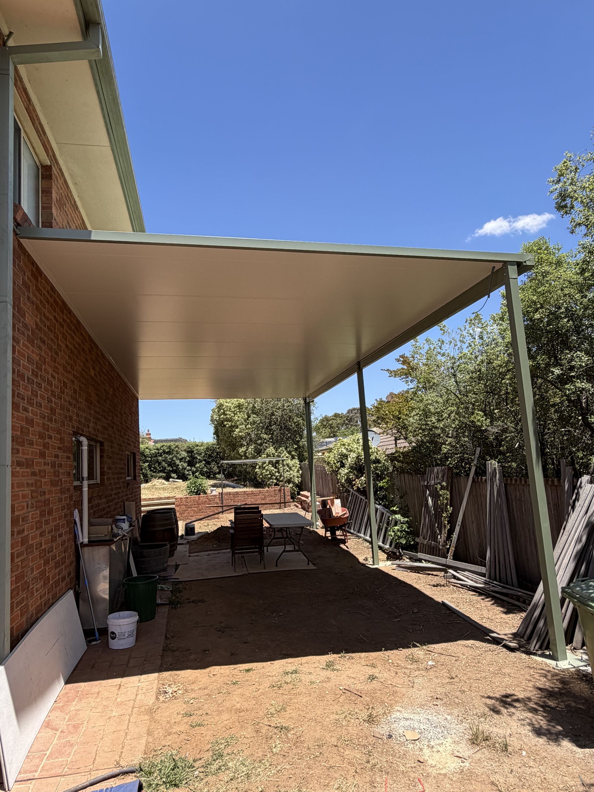 A large, white metal patio roof extends from a brick house over a dirt ground area on a sunny day — Straight up Building Projects in Narrabundah, ACT