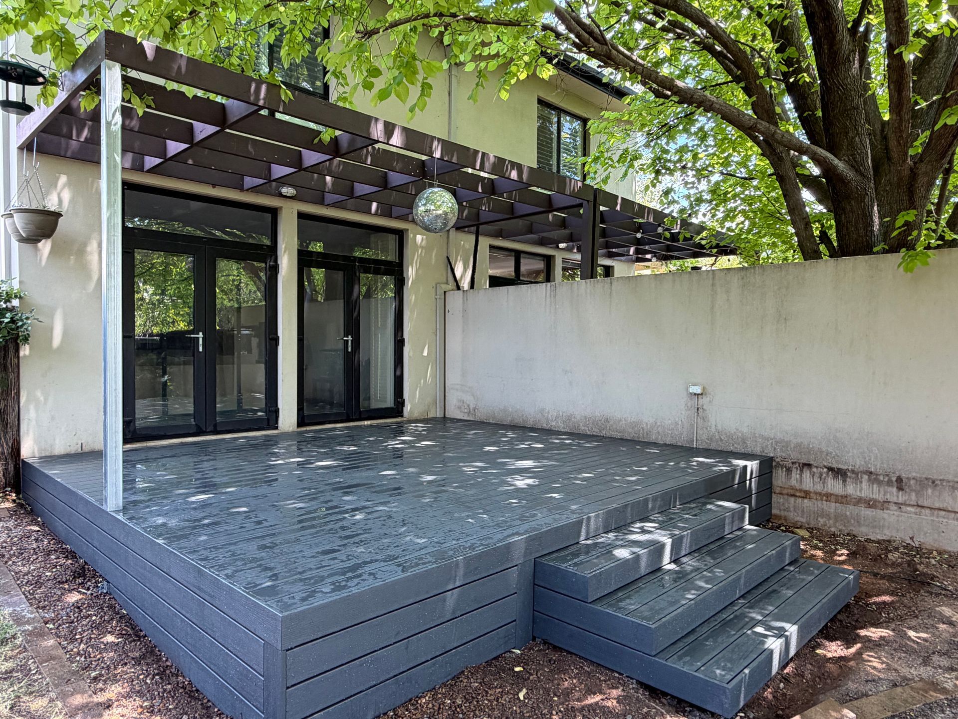 Gray composite deck with steps, connected to a building with black doors under a pergola. — Straight up Building Projects in Holt, ACT