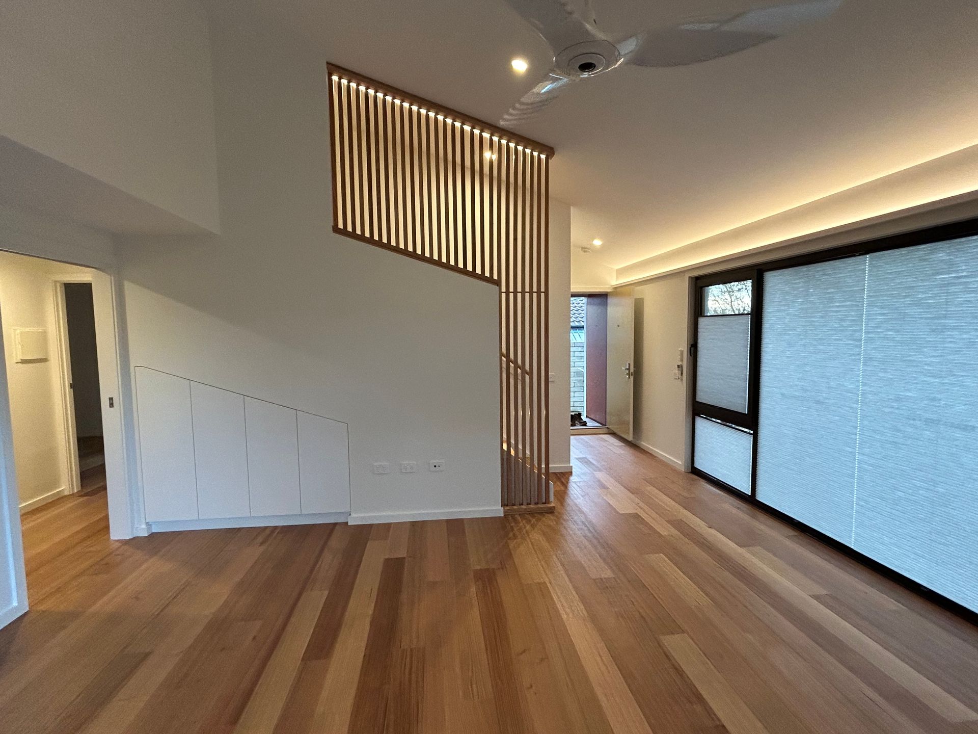 A spacious room with light hardwood floors, a wooden slat room divider, and a large window wall with white roller blinds — Straight up Building Projects in Holt, ACT