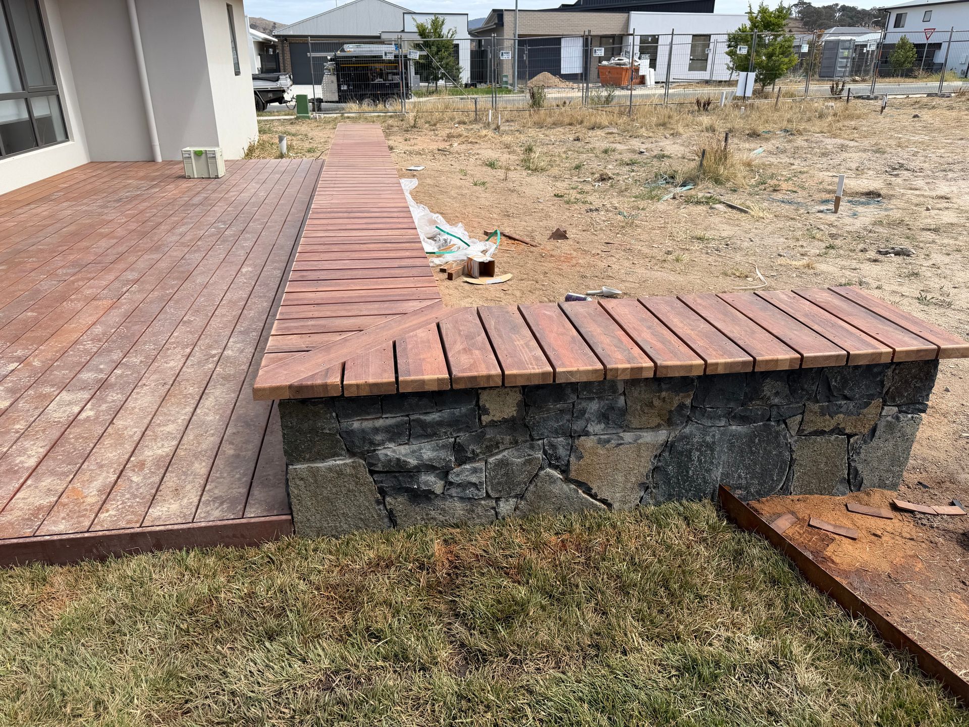 Wooden deck with a stone and wood retaining wall. Dry grassy yard. — Straight up Building Projects in Holt, ACT