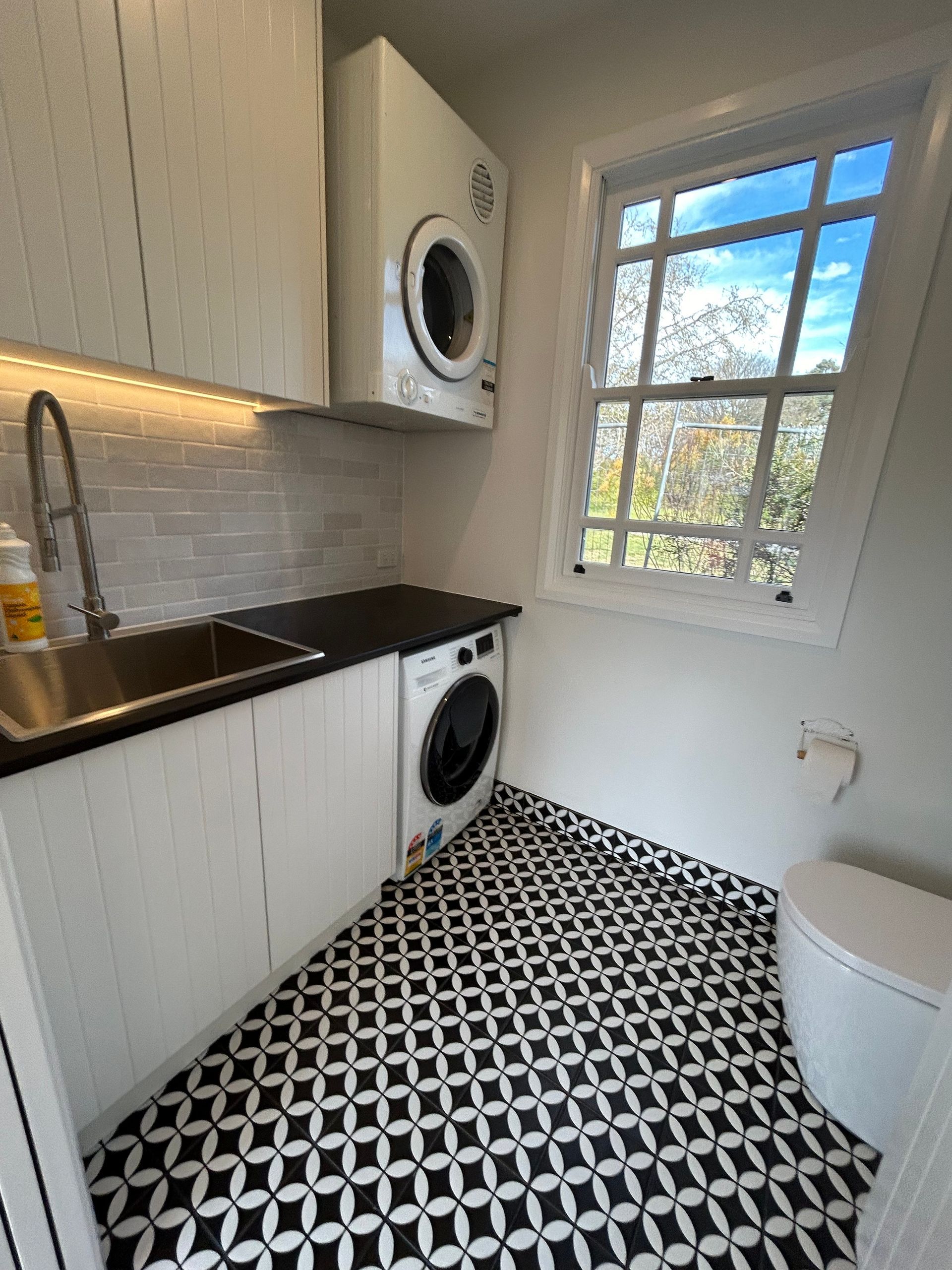 Laundry room with black and white patterned floor, white cabinets, and a washing machine and dryer. — Straight up Building Projects in Holt, ACT