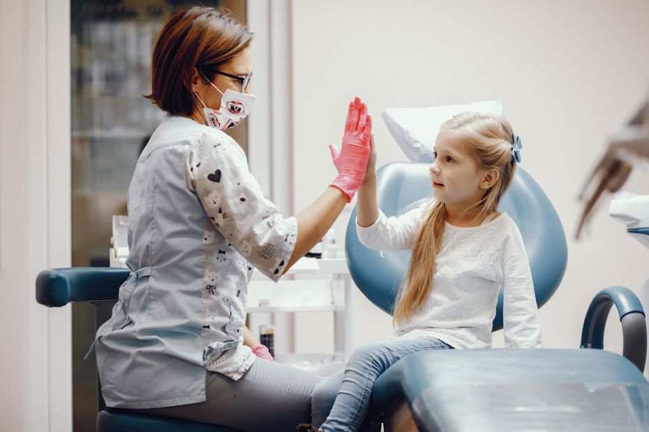 Un paziente odontoiatrico dà il cinque a un dentista in clinica, entrambi indossano dispositivi di protezione.