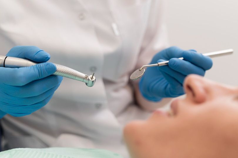 Dentista con guanti blu che tiene strumenti odontoiatrici vicino alla bocca aperta di un paziente