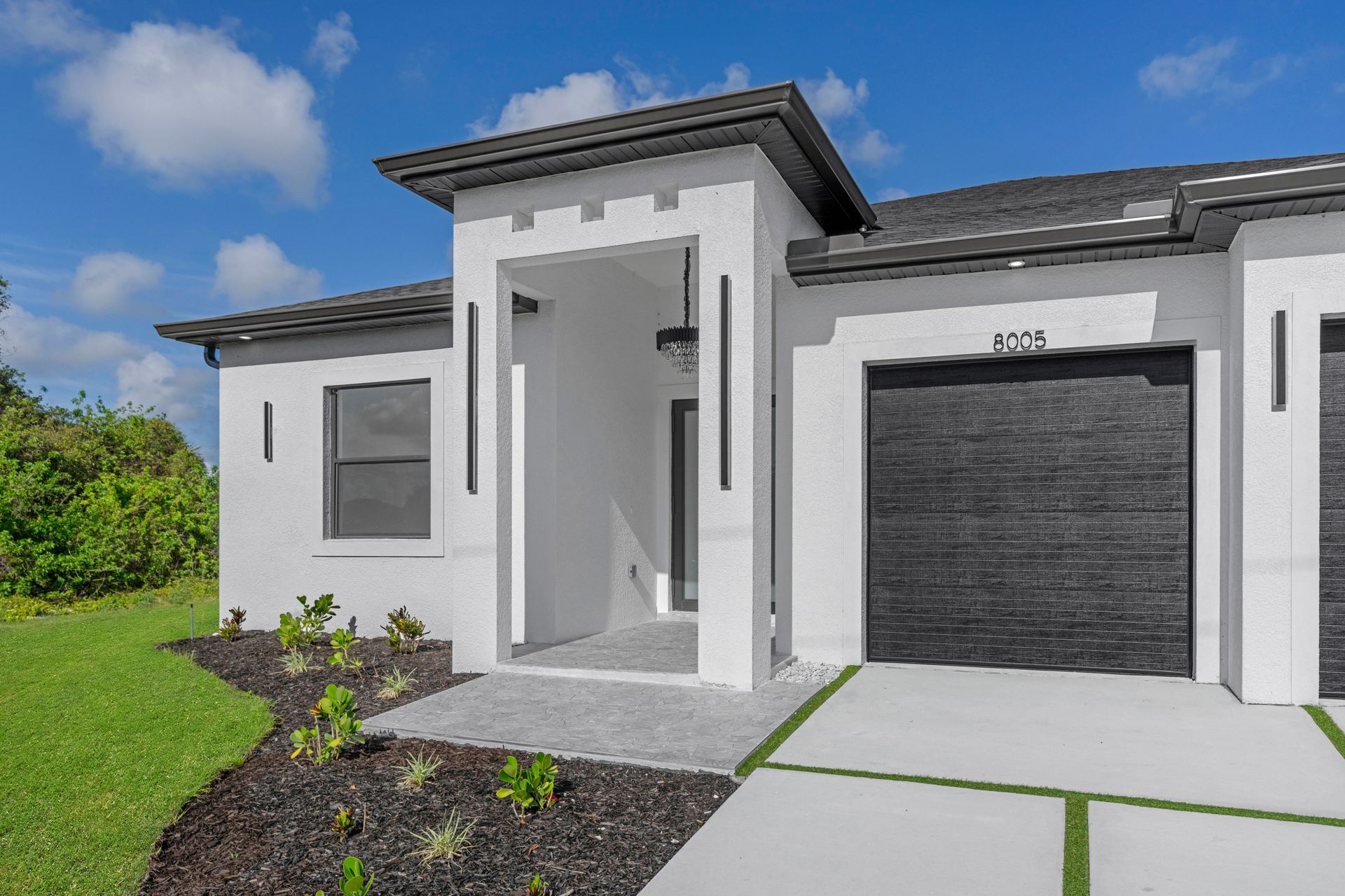 Modern white house with a black garage door and an entryway. Green lawn.