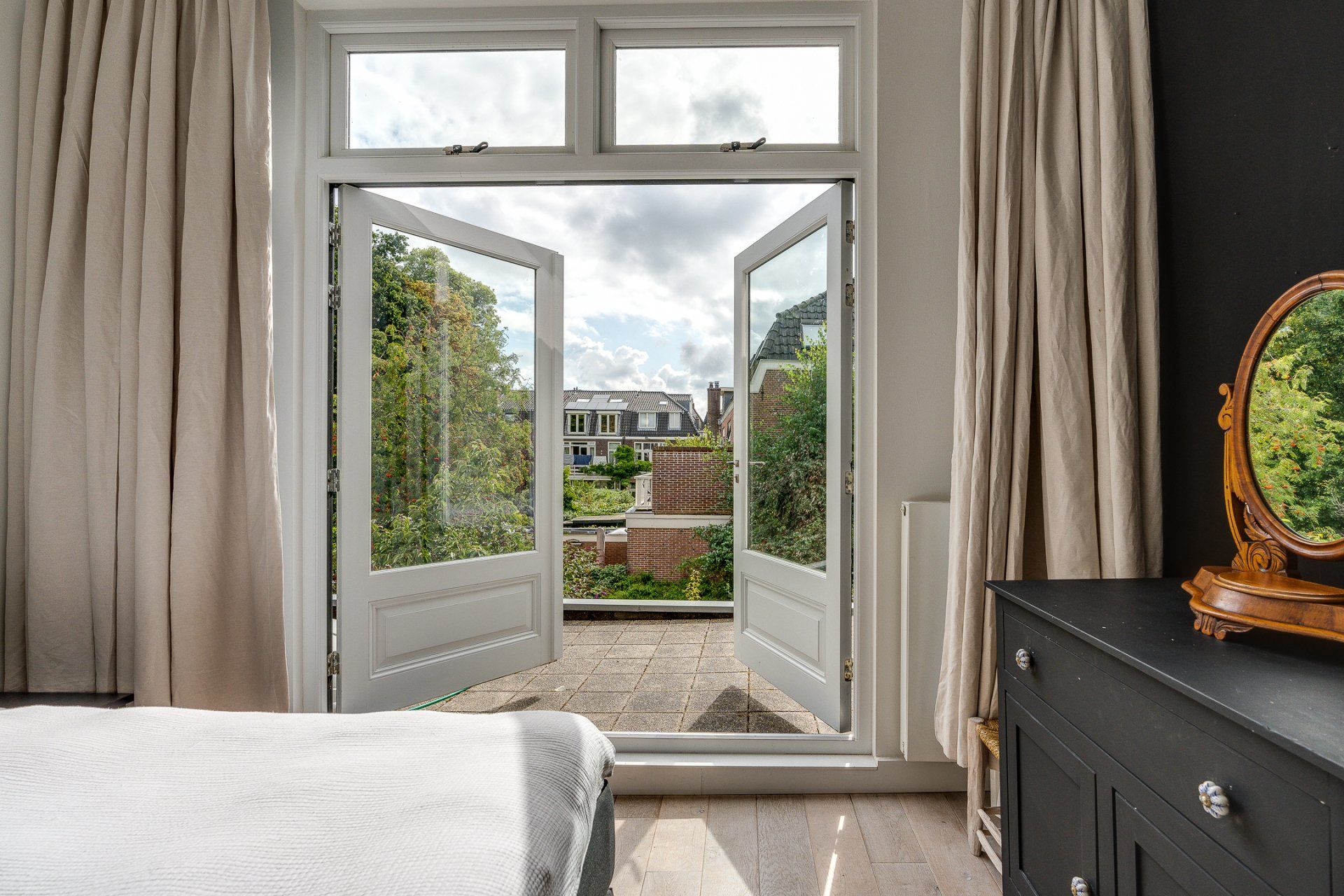 Een slaapkamer met een bed, een ladekast, een spiegel en openslaande deuren naar een balkon.