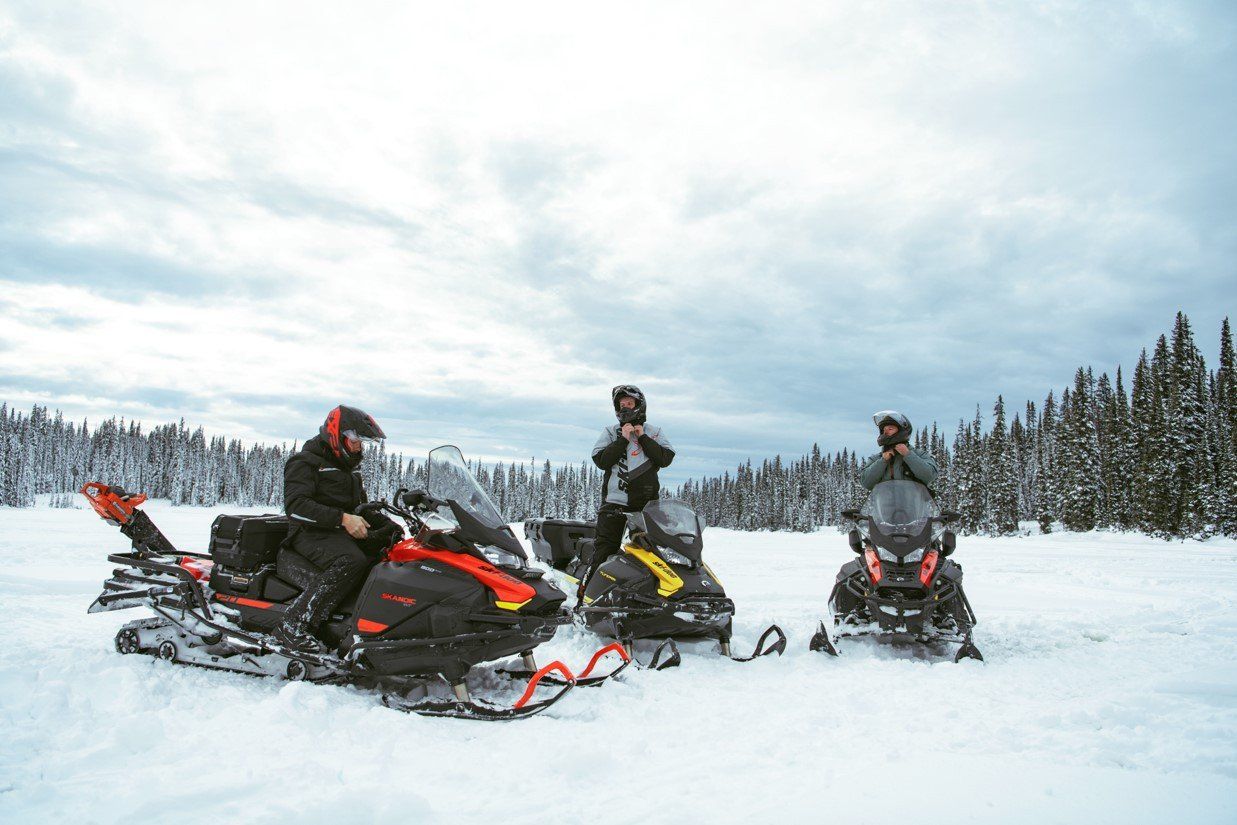 Three people preparing to ride a snowmobile