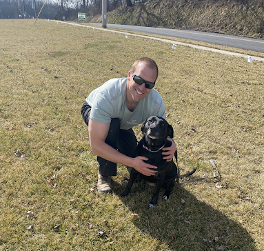 A man is kneeling down next to a black dog