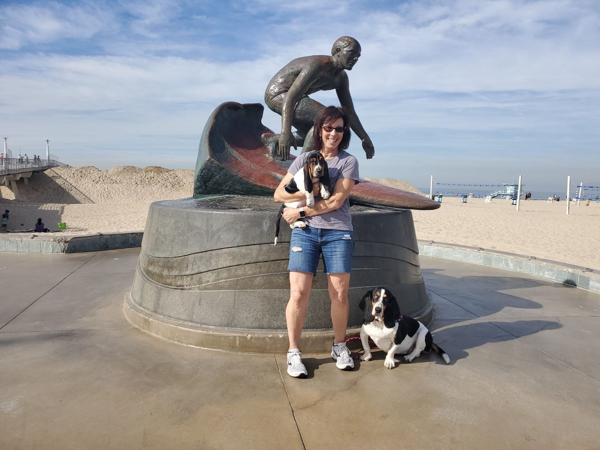 A woman and a dog are standing in front of a statue on the beach.