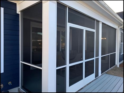 Screened porch with white-framed sliding glass doors and blue siding beside a wooden deck.
