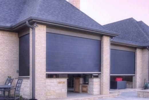 Suburban brick house with large closed window shutters and a patio with bins and chairs