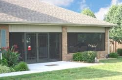 Single-story house exterior with a glass front door, brick wall, and green lawn