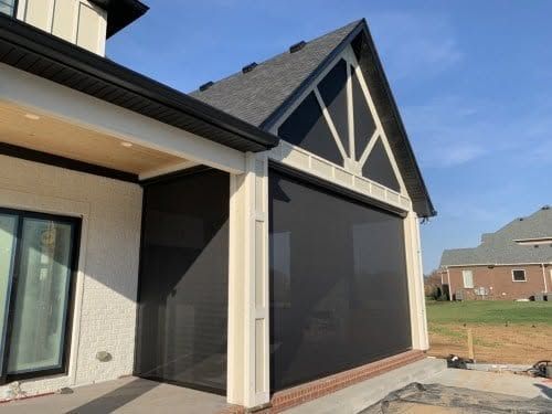 Screened patio attached to a house with beige siding and dark trim under a gabled roof