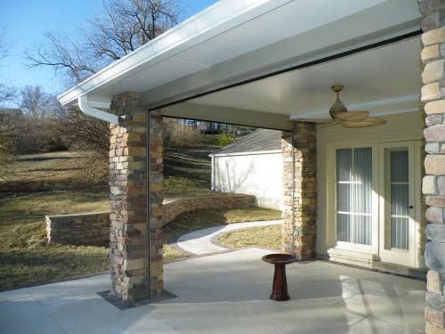 Covered patio with stone columns, sliding glass doors, and a ceiling fan overlooking a yard