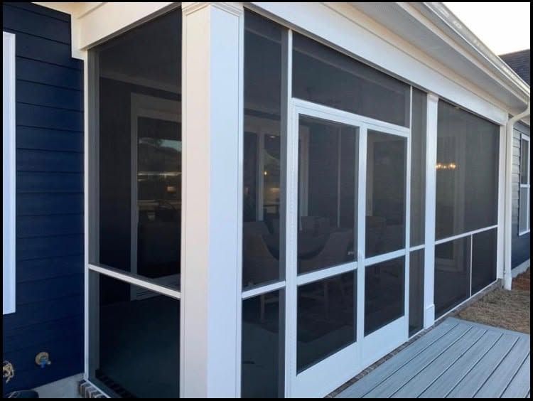Screened porch with white-framed glass doors and dark blue siding beside a wooden deck