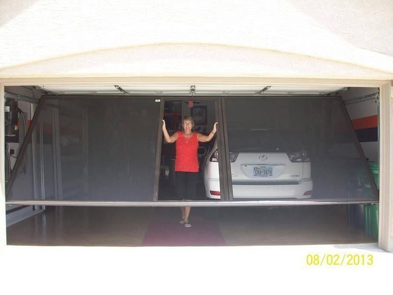 Woman standing in an open garage doorway beside a white car, holding the overhead door rails