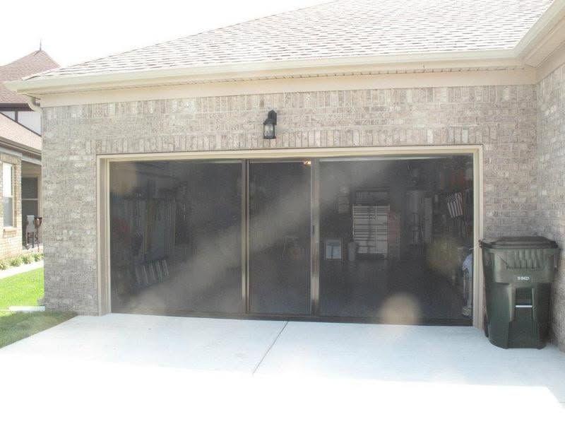 Brick house garage with a dark double garage door and a trash bin on the right