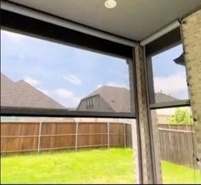Covered patio view of a fenced backyard with green grass and neighboring houses under a partly cloudy sky