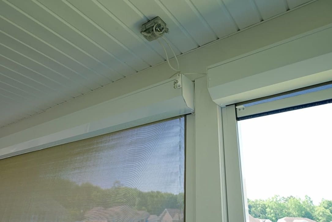 Covered porch ceiling with a small light fixture and white support beams overlooking a screened view outside