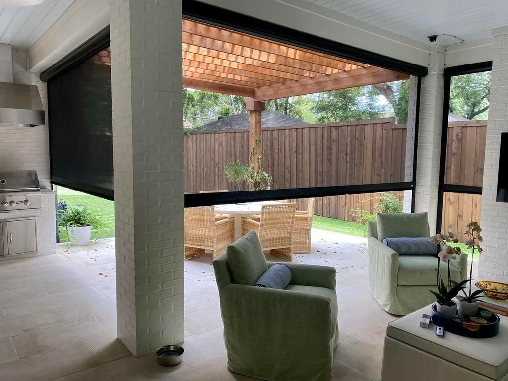 Covered patio with green chairs and a wicker sofa facing a fenced backyard, viewed from indoors