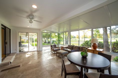 Bright sunroom with large windows, wicker seating, round table, and open view to a patio and garden.