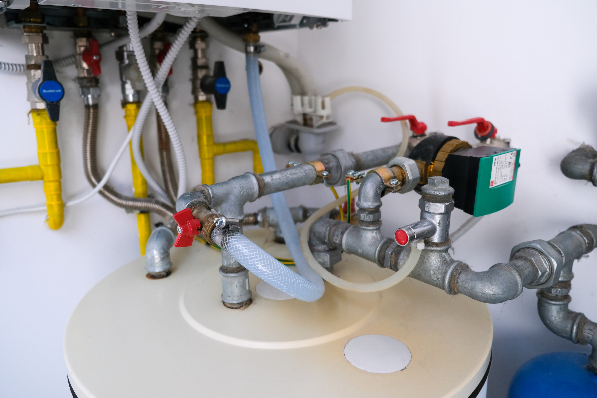 Under-sink plumbing with pipes, valves, and hoses connected to a water heater or tank.