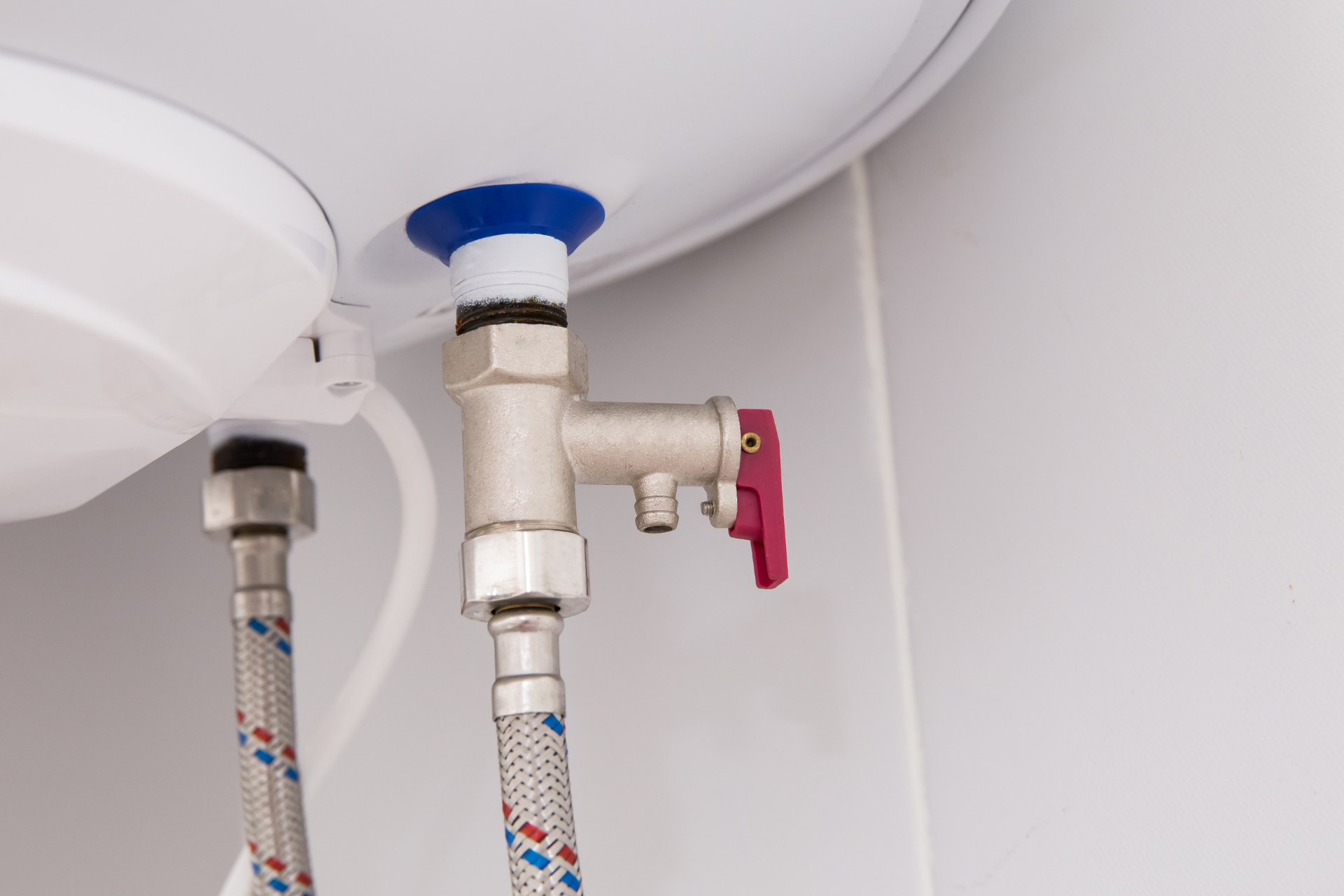 Under-sink plumbing with two braided water lines and a red shutoff valve