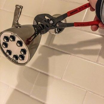 Person using pliers to remove a chrome showerhead from a white tile wall.
